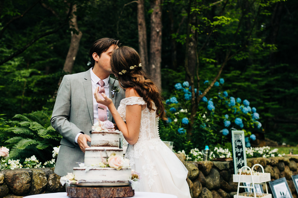 bride kissing groom at cake cutting with a naked cake in a garden