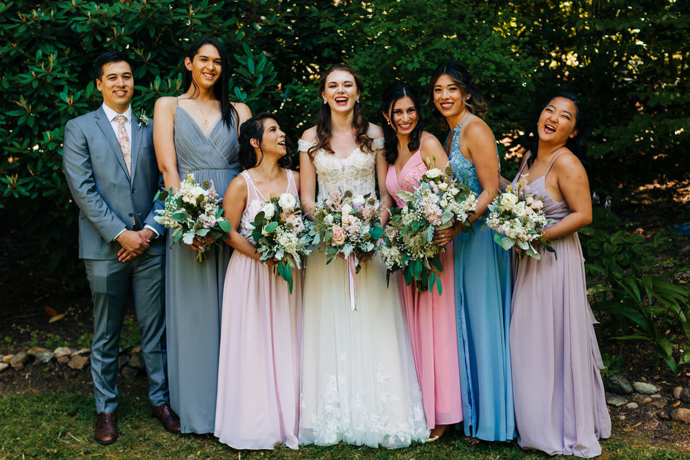 Bride laughing with bridal party in pastel blue and purple dresses