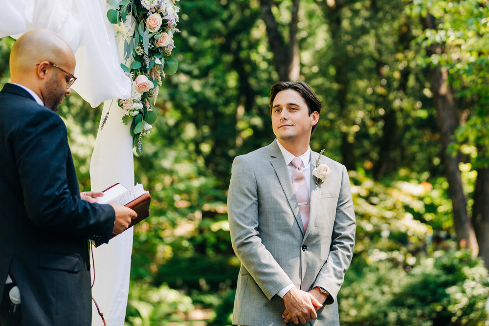 groom waiting before the ceremony begins next to a fabric and floral arch