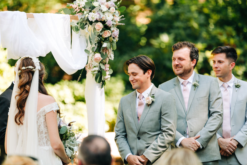 Groom laughing during ceremony with groomsmen in gray suits during outdoor ceremony
