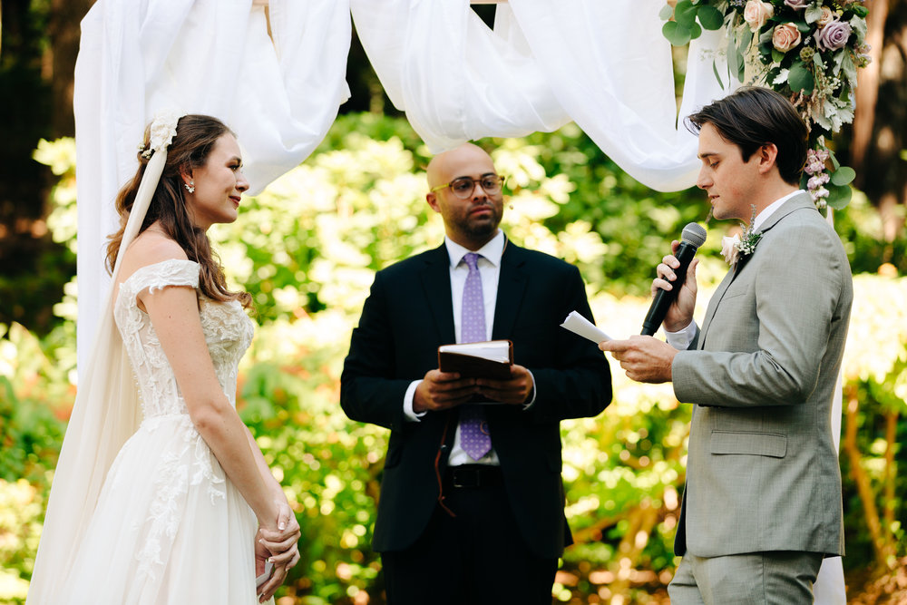 Groom reading vows to bride in outdoor sunny ceremony