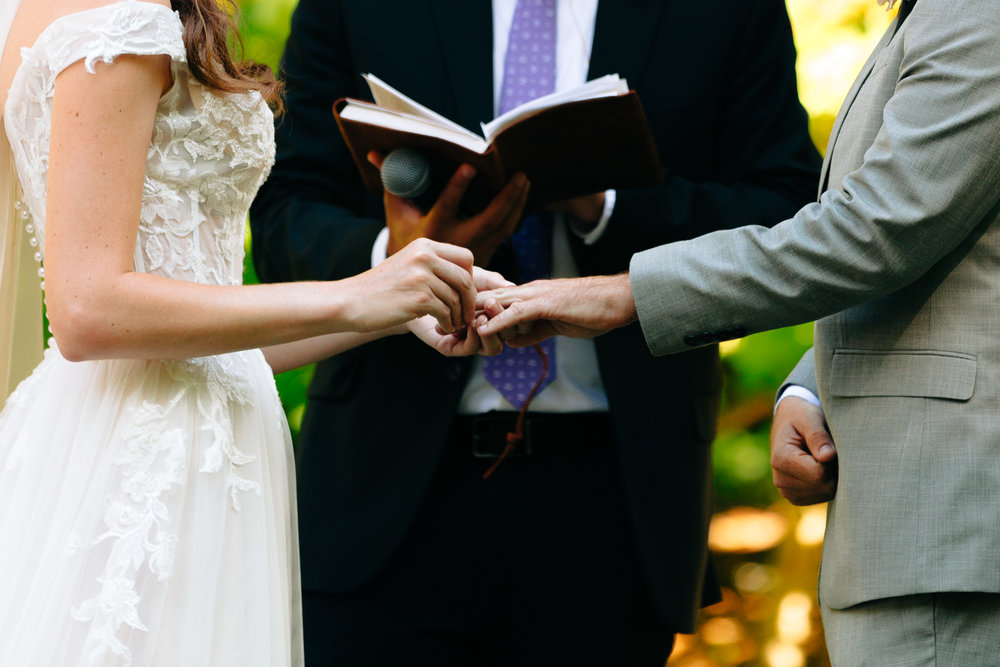 close up of couple's hands exchanging rings at an outdoor ceremony