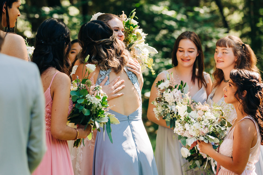 bride hugging a bridesmaid with her bridal party looking after a ceremony