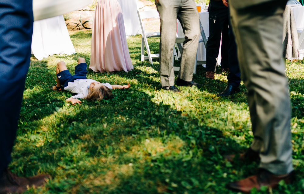 documentary shot of young boy laying in grass surrounded by adults during cocktails