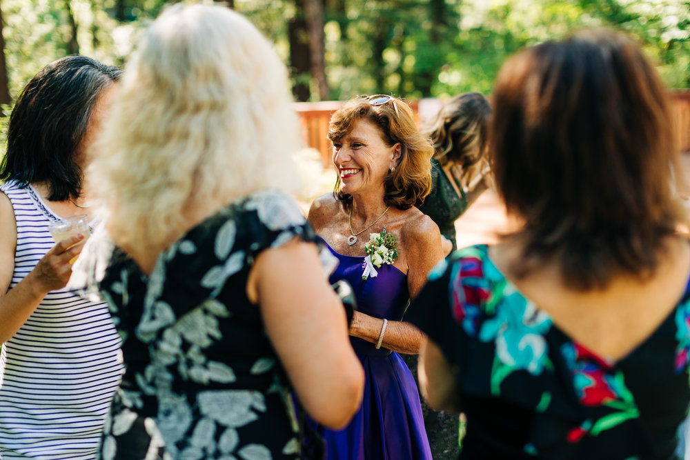 mother of groom in purple dress with pockets laughing with guests