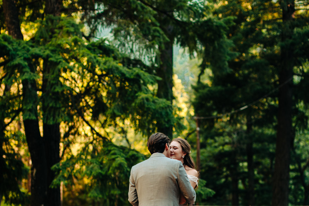 first dance of couple looking at each other against tall green treeline