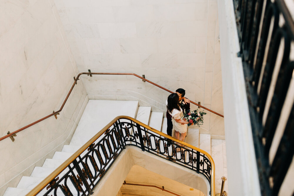 couple stops at the end of a staircase at city hall for a quiet kiss