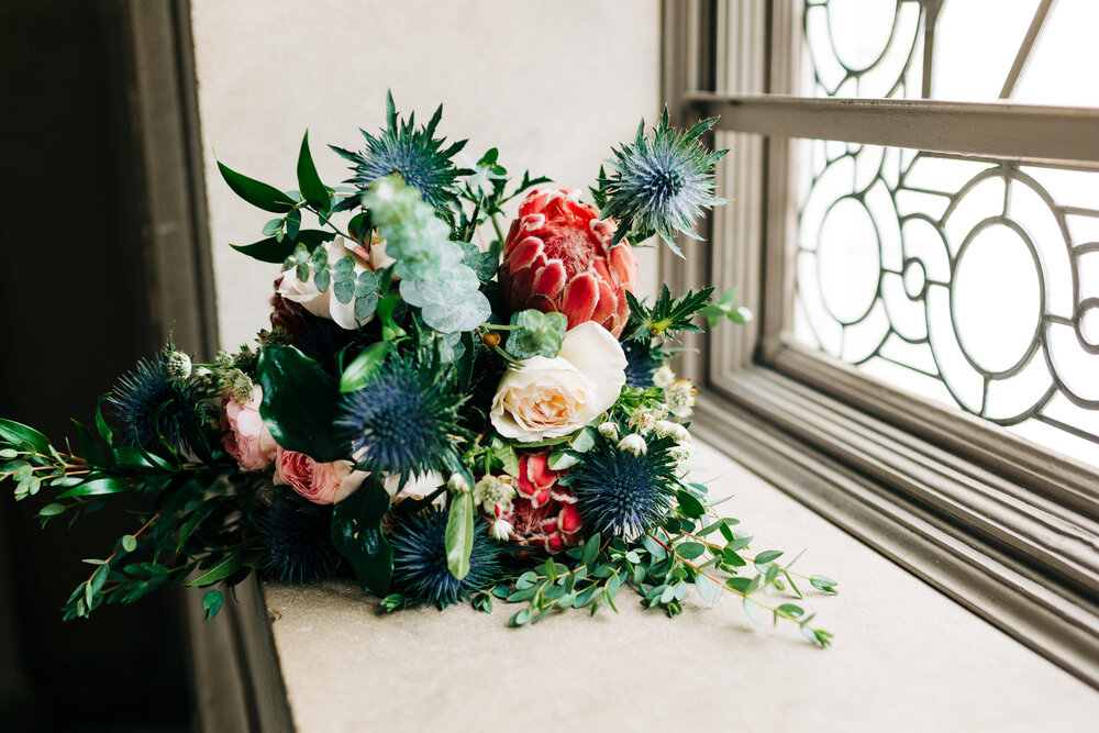 Bouquet of greenery with blue thistle and pink flowers in front of art-deco windowsill