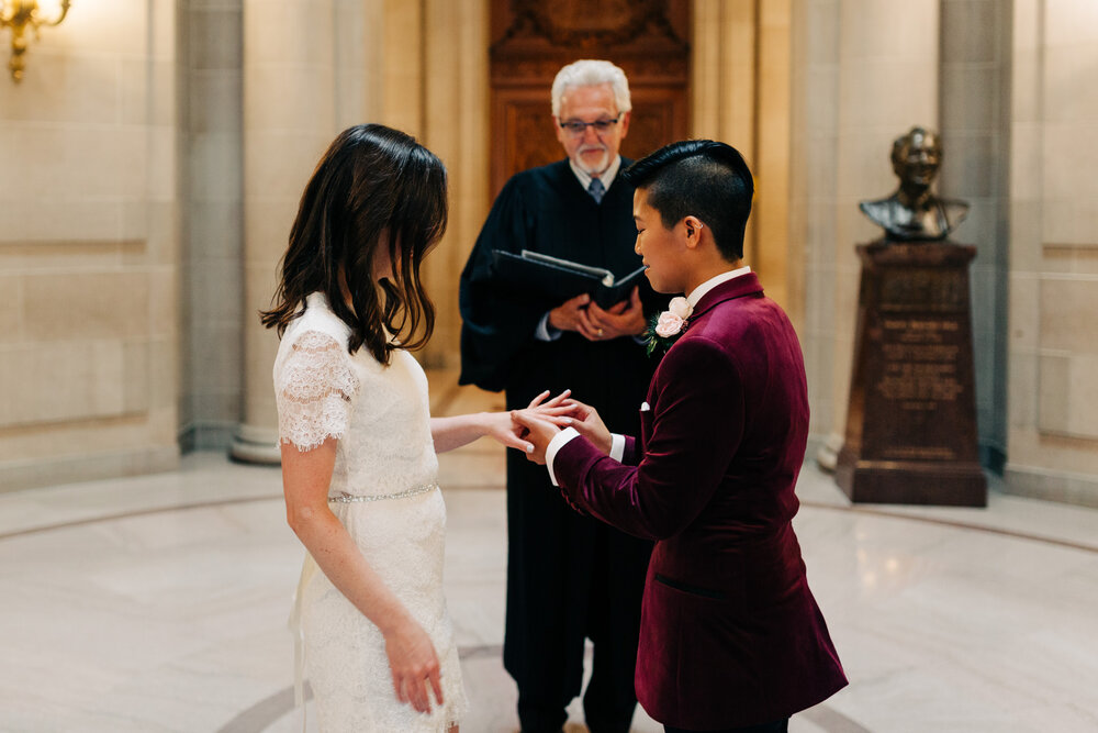one marrier putting a wedding band on her partner in front of a city hall officiant in the rotunda