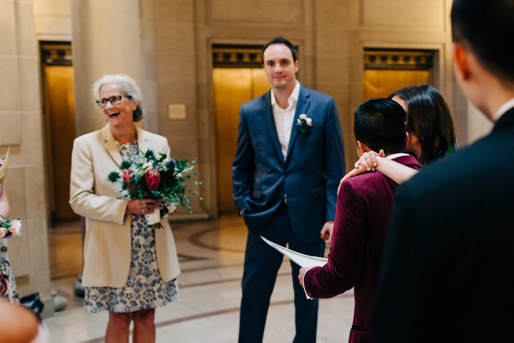 candid moment of mother of  bride holding bouquet and couple hugging