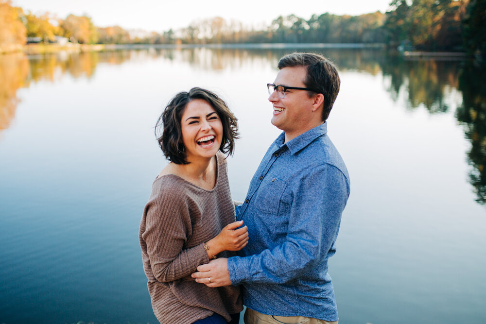 couple in fall attire laughing next to a lake