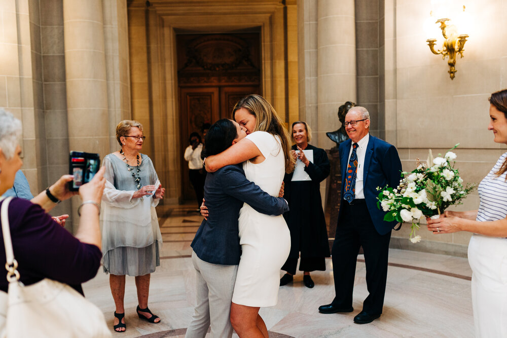 Two marriers have their first kiss in the rotunda surrounded by parents and friends
