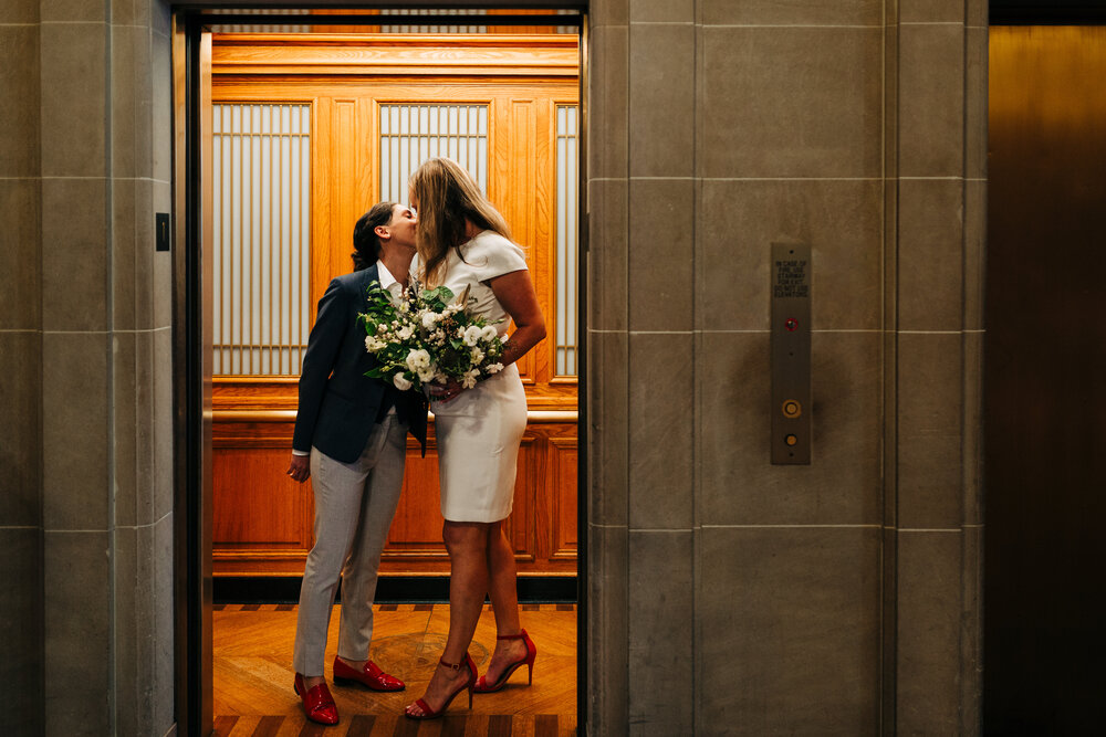 Two brides sneak a kiss while getting on an elevator