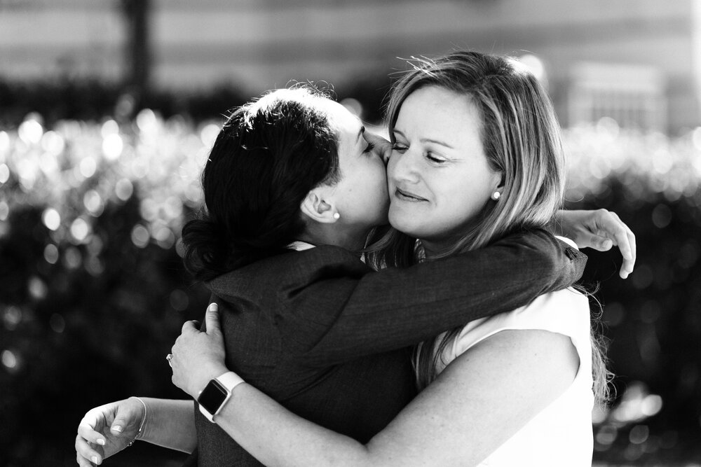 Two marriers embrace in a black and white candid photo, one giving the other a kiss on the cheek