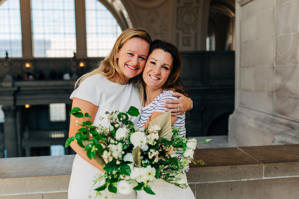 A formal portrait of a bride hugging her best friend on her wedding day and holding a bouquet