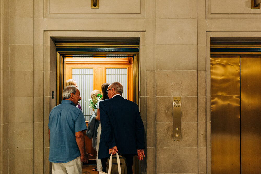 Two marriers’ fathers step into the elevator on the way to the marriage license office