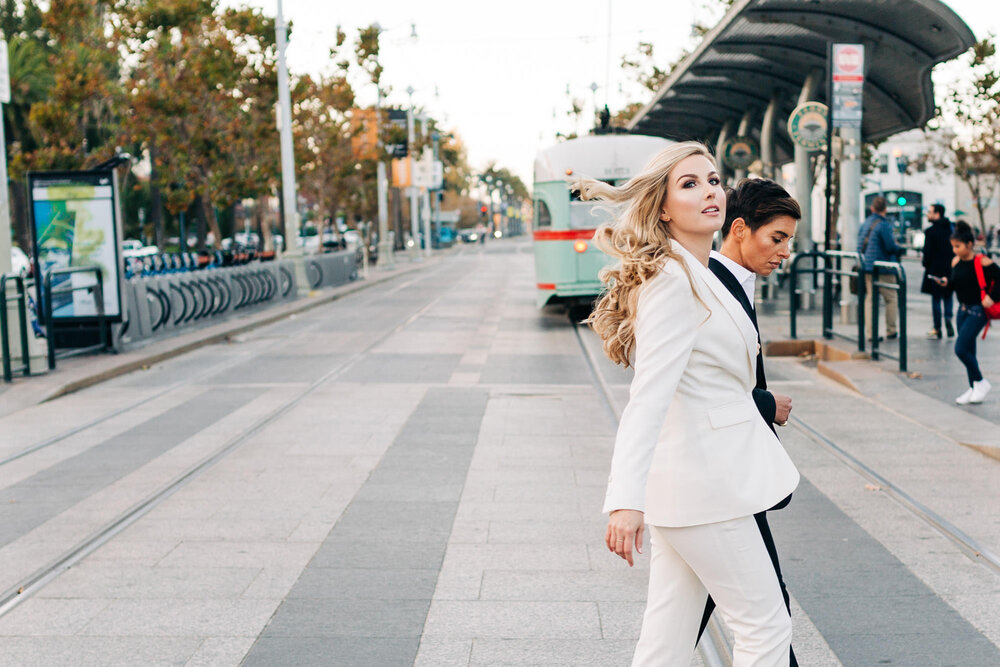  Couple in tuxes walking past a trolley in front of the San Francisco Ferry Building at their Embarcadero elopement 