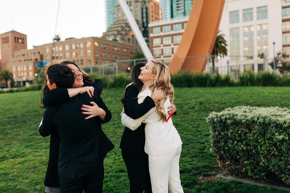  Officiant and witness hug two brides at their Embarcadero elopement at Cupid’s Span 