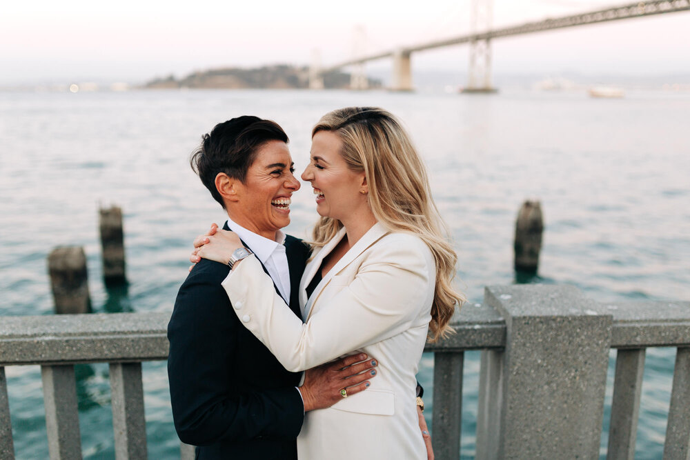  Newly married couple holds each other in front of the San Francisco Bay Bridge 