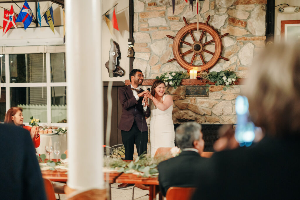 candid photo of a wedding couple laughing while making a toast at their yacht club reception