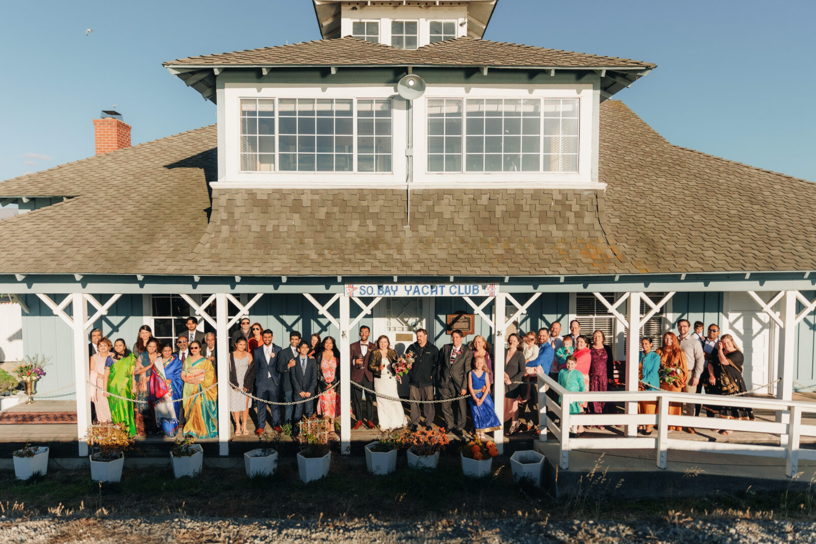 large group photo of all wedding guests together on a front porch of a blue yacht club