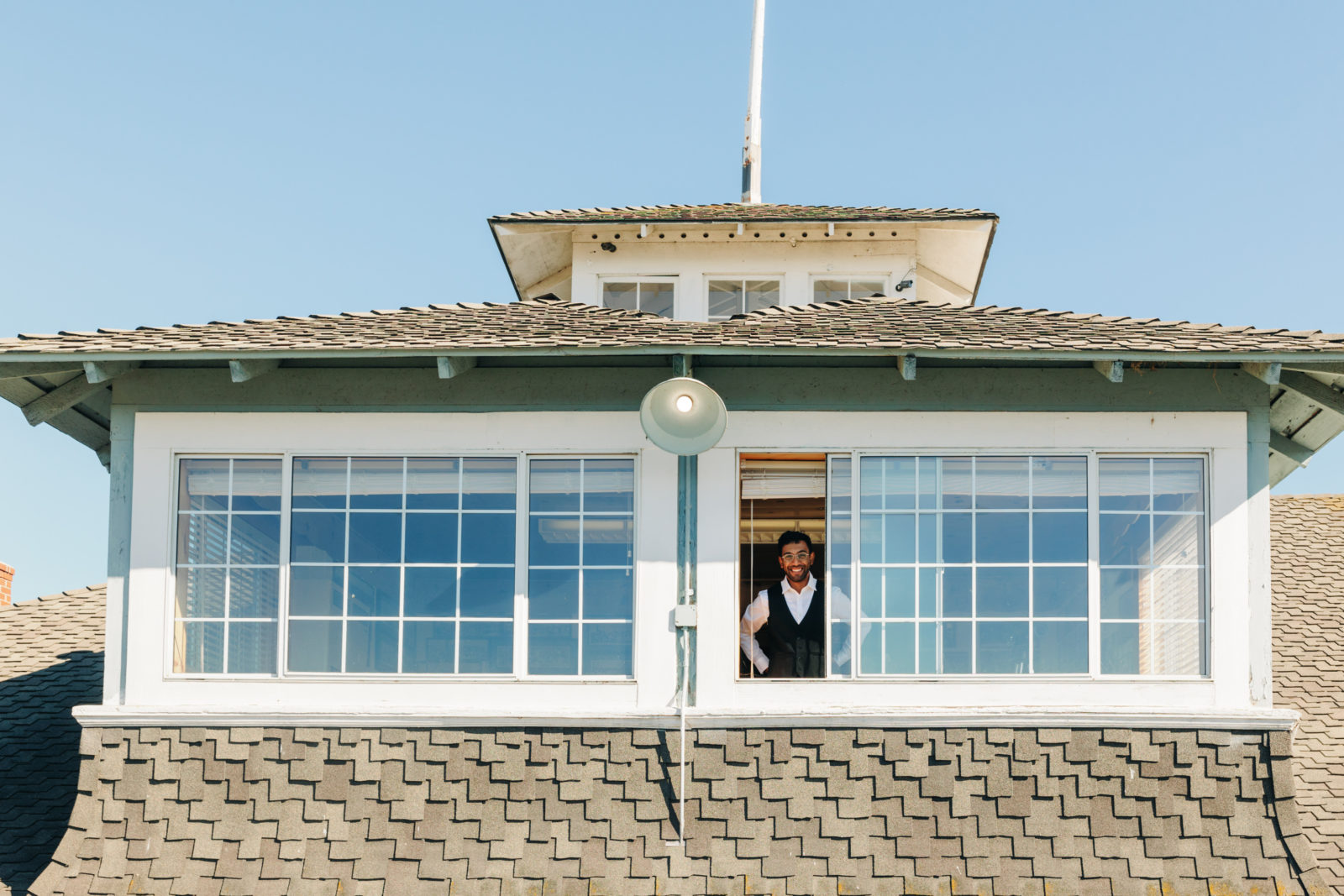 Candid photo of groom smiling through large windows while getting at a yacht club