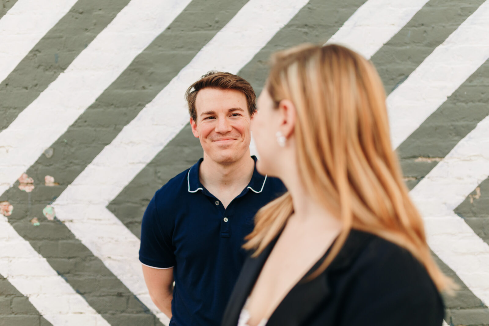 An engaged couple smiling at each other in front of a mural along South Main Street in Memphis, featuring one partner in the background