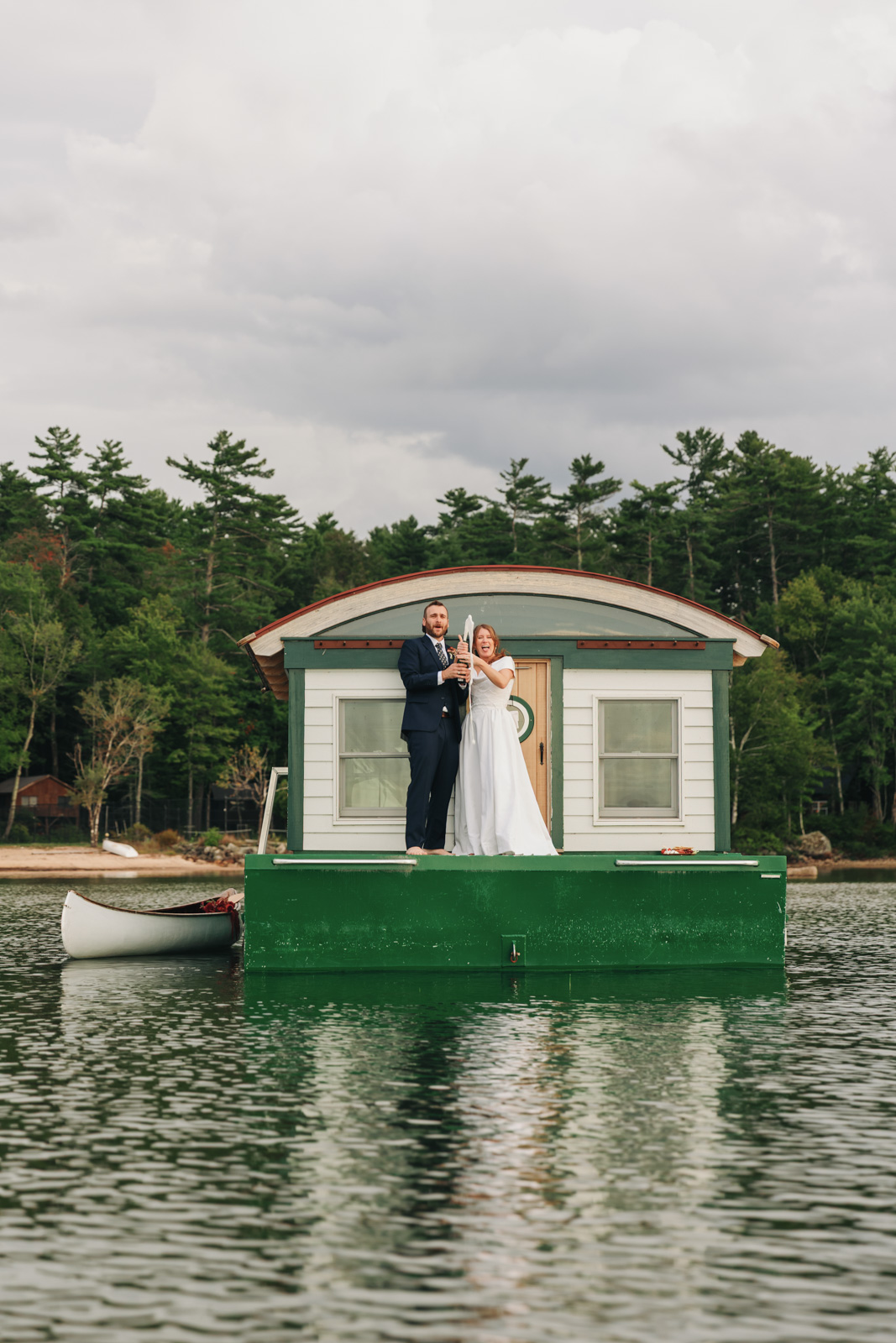Newlyweds pop champagne off of a houseboat at their New England summer camp wedding